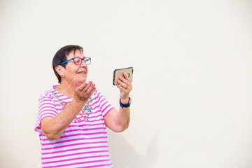 mujer mayor sonrie saluda con la mano videollamada con telefono movil aislada en fondo amarillo - obrazy, fototapety, plakaty