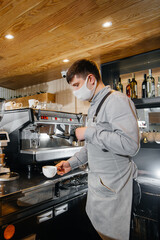 A masked barista prepares delicious coffee at the bar in a cafe. The work of restaurants and cafes during the pandemic.