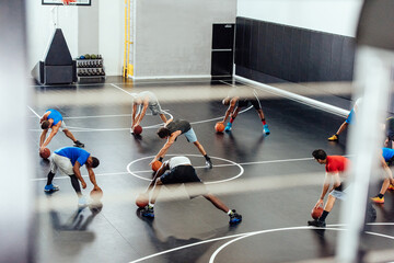 Male trainer and basketball players warming up stretching forward on court © Image Source Limited