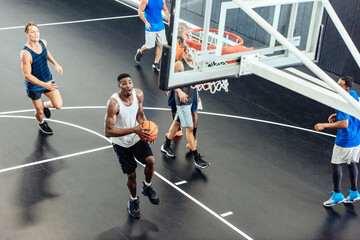 Male basketball team throwing ball into hoop on basketball court © Image Source Limited
