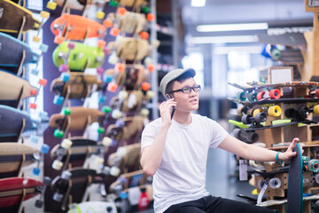 Fototapeta na wymiar Young male skateboarder making smartphone call in skateboard shop