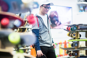 Young male skateboarder looking at skateboards in skateboard shop