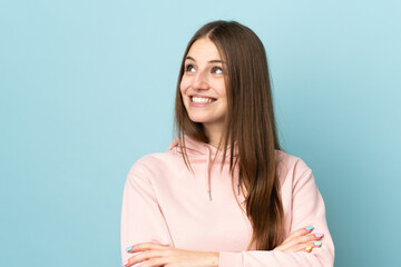 Young caucasian woman isolated on blue background looking up while smiling