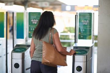 Rear view of woman using ticket touchscreen at railway ticket barrier