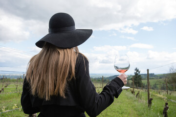 Woman standing in vineyard, holding glass of wine, rear view