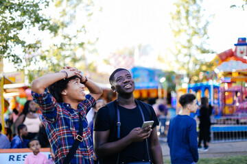 Two friends at funfair, looking up, laughing