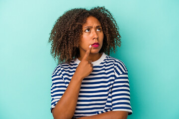 Young african american woman with curly hair isolated on blue background looking sideways with doubtful and skeptical expression.