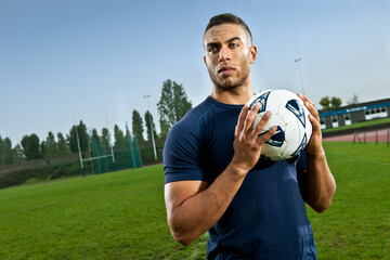 Soccer player holding football on pitch © Image Source Limited