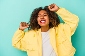 Young african american woman with curly hair isolated on blue background celebrating a special day, jumps and raise arms with energy.