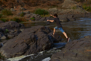 Obraz premium guy traveler jumps over the rocks over a mountain river. travel and ecotourism concept. High quality photo