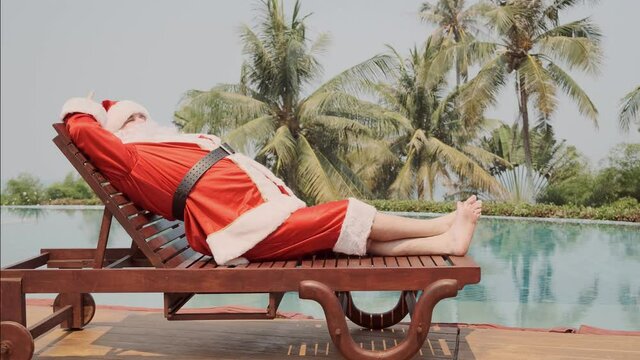 Happy Santa sunbathes on deckchair near swimming pool on sunny day. santa claus on rehabilitation on vacation.