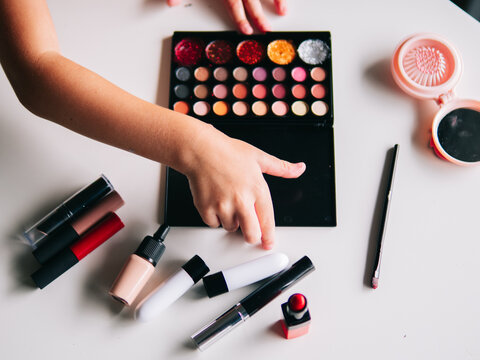 Crop child with assorted cosmetic products on table