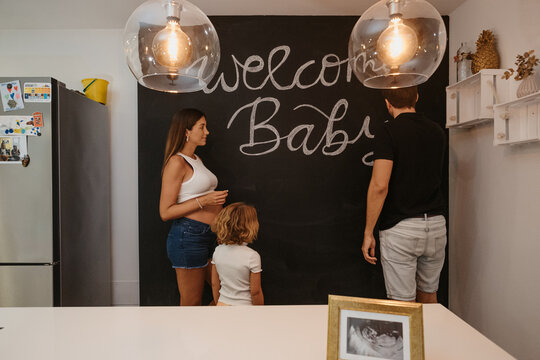 Man writing Welcome Baby title on chalkboard against pregnant wife