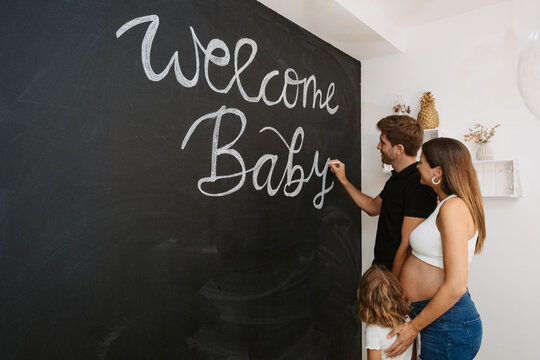 Man writing Welcome Baby title on chalkboard against pregnant wife