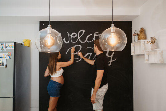Man writing Welcome Baby title on chalkboard against pregnant wife