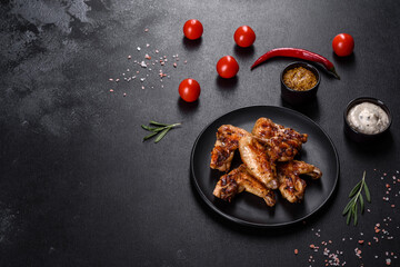 Grilled spicy chicken wings on a dark background with spices and herbs