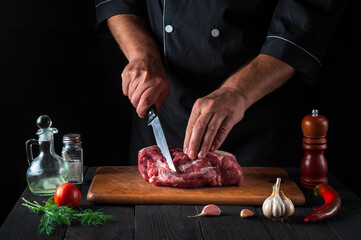 Professional chef cuts meat with a knife in the kitchen prepares food. Vegetables and spices on the kitchen table in a restaurant to prepare a delicious lunch