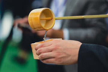 Details with the hands of a man pouring traditional Japanese sake in a wooden cup.