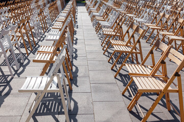 Folding chairs are arranged in the area for outdoor activities . Rows of empty folding wooden chairs in a public square before spectators and guests arrive.