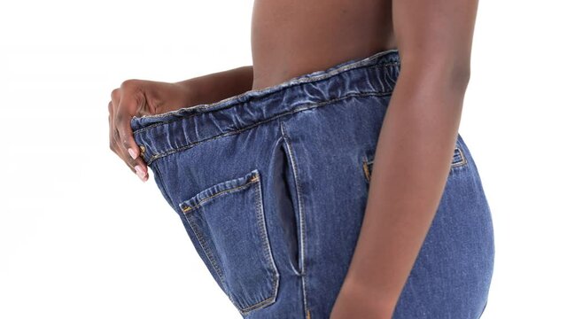Close up of an African woman showing her weight loss in old, oversize jeans. Isolated on a white background.