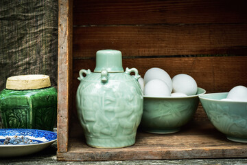 Celadon green Asian style ceramic bottle and bowls filled with white eggs inside vintage wooden box still life - 456592050