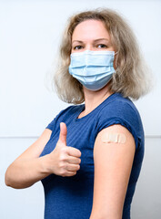Vaccinated young woman showing shoulder with plaster. COVID-19 vaccine concept.