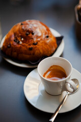 The table with sweets (pastries: croissant, cookies), white cups (mug) with hot black coffee (espresso), the saucer, the spoons at a local bar. Traditional Italian breakfast. Milan, Lombardy, Italy