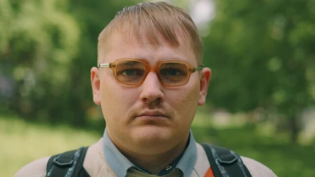 Portrait of serious nerdy man in glasses. A loser teenager is looking to the camera.