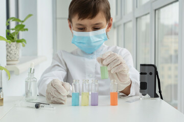 Schoolboy in protective clothers is ready for chemical experiments with liquids in different test tubes, scientific concept