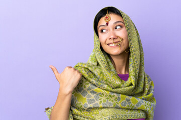 Indian woman isolated on purple background pointing to the side to present a product