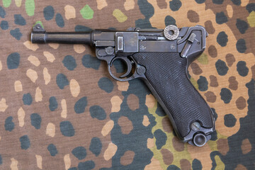 German Parabellum pistol on the background of military camouflage. Reconstruction of the combat...