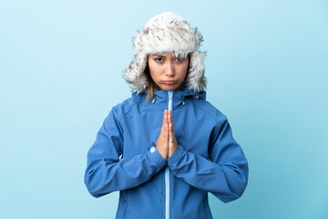 Young Uruguayan girl with winter hat isolated on blue background pleading