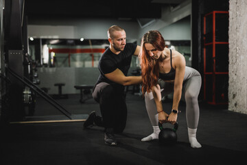 Fototapeta na wymiar Muscular Woman Doing Kettlebell Training With Personal Trainer At The Gym