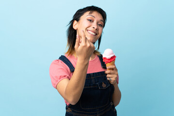 Young Uruguayan girl holding a cornet ice cream over isolated blue background inviting to come with...