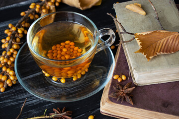 sea ​​buckthorn drink, star anise and old books on dark background