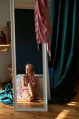 Dreamful pink haired lady listens to music reflecting in large mirror in bedroom