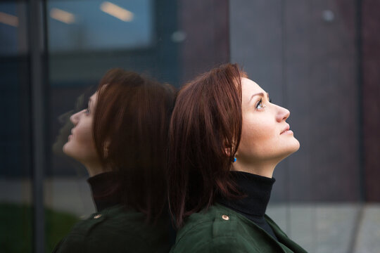 A brunette woman with a bob haircut stands with her back to the mirrored wall, is reflected and looks sad. The theme of loneliness