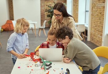 Engaged in process. Concentrated kids learning how to build robotic toys and programming them using computer during STEM class with young female teacher