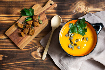 Pumpkin soup in a bowl with seeds and parsley on a wooden background. Crackers with spices on the board. Copy space. Thanksgiving, autumn soup