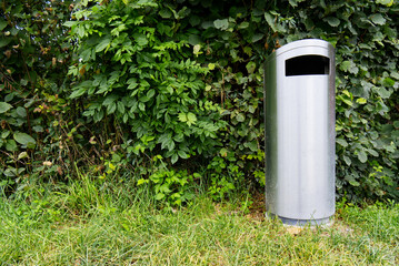 
Silver trash can on a green meadow with green bushes in the background
Silver trash can on green field with green bushes in background
