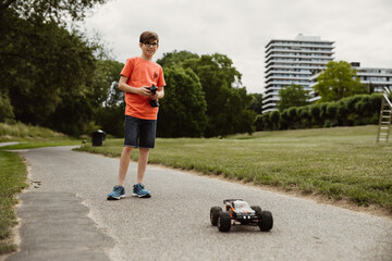teen boy with electric remote control car toy play outdoor on sidewalk and have fun while enjoy his...