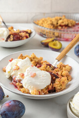 Fruit crumble. Plum crumble pie with vanilla ice cream in plates with spoons on white marble table for tasty breakfast.