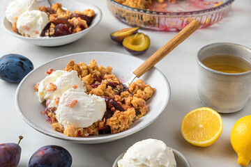 Delicious dessert . Plum crumble pie with vanilla ice cream in plates with cup of tea on white marble table for tasty breakfast