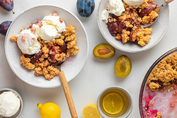 Plum crumble pie dessert with vanilla ice cream in plates with cup of tea on white marble table for tasty breakfast