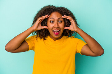 Young african american woman with curly hair isolated on blue background receiving a pleasant surprise, excited and raising hands.