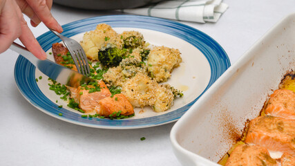 Fresh baked salmon fillet and baked vegetables served with chives close up on plate on white kitchen table