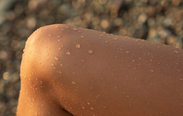 Tanned black woman  legs with water drops lie on the beach.