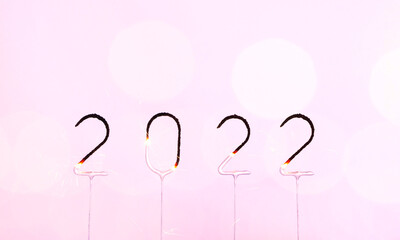 2022 burning sparklers number on pink background with blurred bokeh light. Happy New Year and Merry Christmas banner with copy space. Template holidays for poster, party invite or greeting card