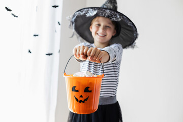 An orange pumpkin bucket full of sweets is being held by a charming girl dressed as a witch. Happy...