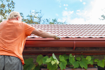 A man cleans out debris and leaves from the gutter system on the roof of his house